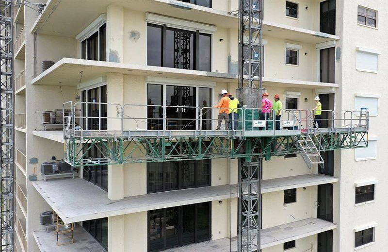 Crew members on a suspended work platform inspecting the balconies of a high-rise condominium